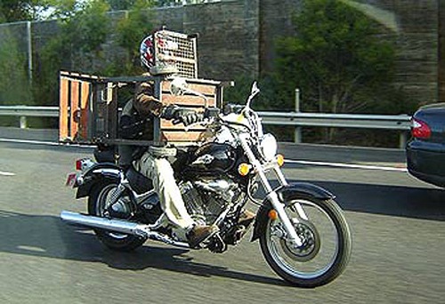 Biker in Australia carrying barbecue. A person rides a motorcycle on a highway, transporting a barbeque grill. He is looking through a rack that is fully in front of his helmeted head.