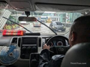 Driver in a car navigating a flooded road during rain, seen from the rear seat.
