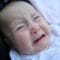 A baby with light skin and light brown hair is crying loudly with his mouth wide open. Tears are on its cheeks, and its eyes are squeezed shut. The background is plain white.