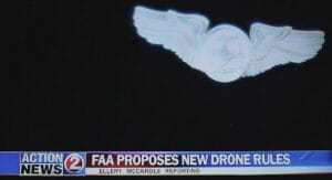 A pair of Drone Pilot Wings against a black shirt -- a photo of a TV screen with text across the bottom from "Action 2 News" illustrating the story 'FAA Proposes New Drone Rules'.