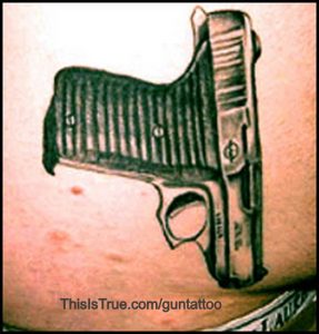 A realistic tattoo of a handgun is inked on someone’s skin, appearing to be tucked into their waistband.