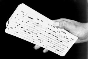 A hand holds a stack of punched cards, used for data storage and programming in early computers. The cards have rows of rectangular holes punched in patterns.