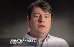 A man with short brown hair wearing a light-colored shirt is shown speaking in a screencap from a TV show. On-screen text reads, JONATHAN METZ, SURVIVOR. The background is dark and out of focus.