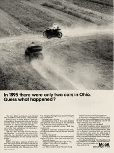 Black and white photo shows two cars at a rural crossroads, kicking up dust. Text below describes how, in 1895, two cars in Ohio crashed, promoting safe driving. Mobil logo appears in bottom right.