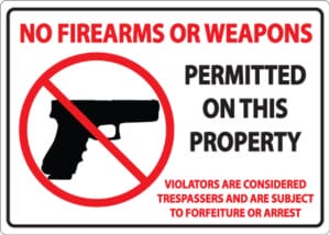A sign with a handgun in a red circle and slash, reading: No firearms or weapons permitted on this property. Violators are considered trespassers and subject to forfeiture or arrest.