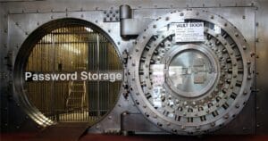 A large, round steel vault door with prominent bolts and a handle. The words “Password Storage” appear on the inner door.