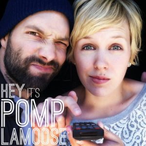 On an album cover, two people stand closely together; a man has a dark beard and wears a beanie, while a woman with short blonde hair holds a remote. Text says: “Hey it’s Pomplamoose.”.