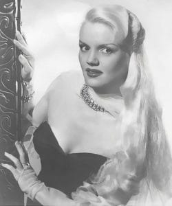 A glamorous woman with long, wavy blonde hair poses in a strapless dress and necklace, looking toward the camera. The black-and-white photo has a vintage, classic Hollywood style.
