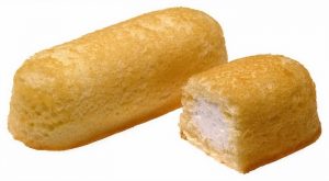 A Twinkie next to another half-Twinkie that has been cut open, revealing the white creamy filling inside.