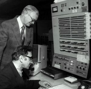 Men in front of large 1960s computer console.