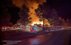 Large single-story building on fire, with firefighters turning their hoses on it.