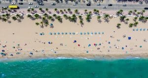 Aerial view of Florida coast with lots of cars and people sunning and swimming, and so small they are just dots.