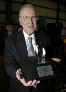 Elderly man holding award.