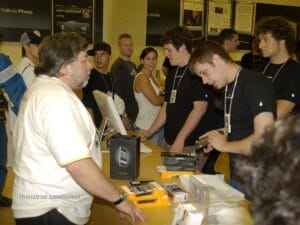 Another angle of the same scene, though here it's more clear that he has several items stacked up, a black "iPhone" bag standing ready to package his purchases. Both angles show quite a few people crowded in the store, with the line still extending well outside the door.